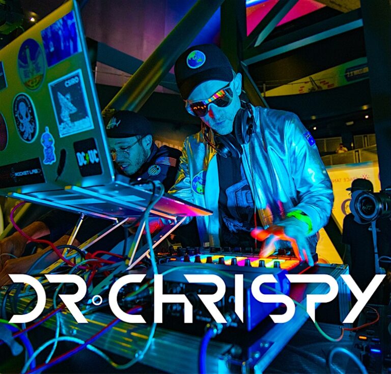 Dr Chrispy plays beats from his laptop in a shiny coat and hat